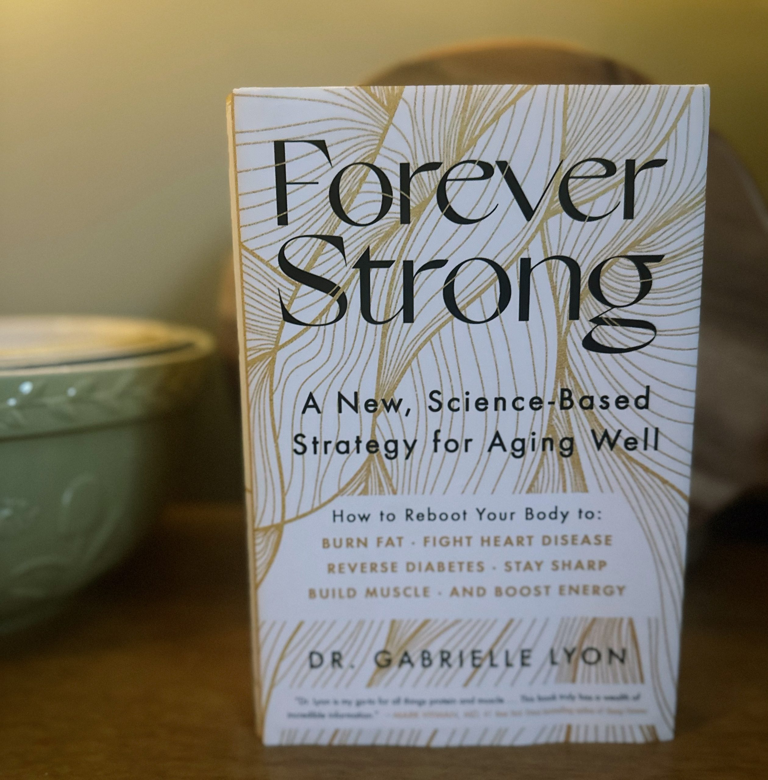 The book "Forever Strong" on a shelf next to a green bowl.