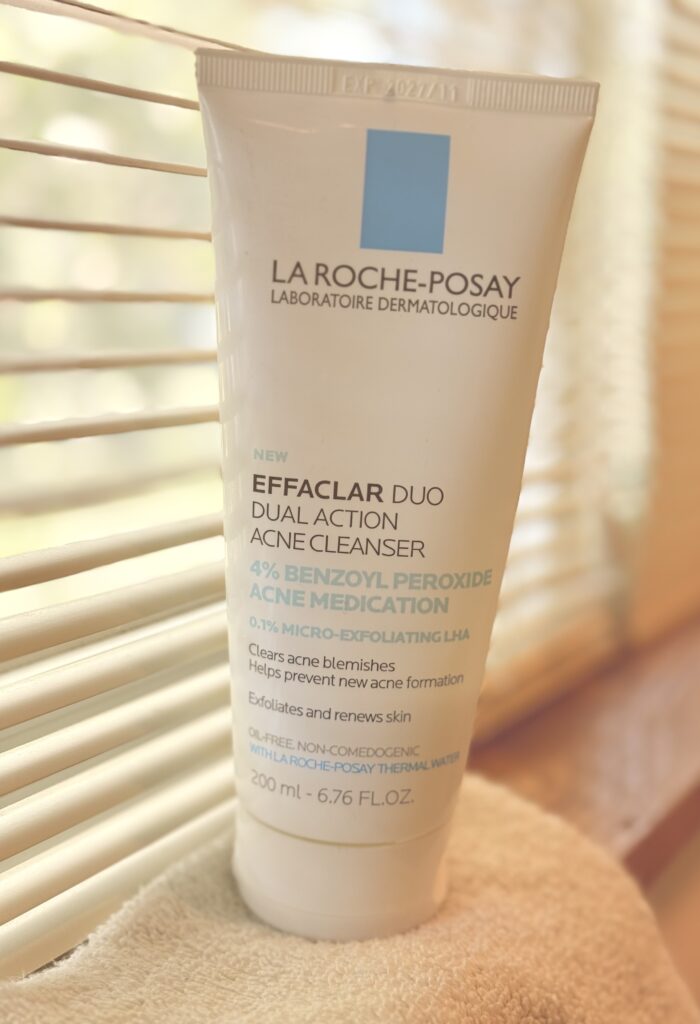 A bottle of La Roche-Posay Benzoyl Peroxide face wash sitting on a sunlit window sill.